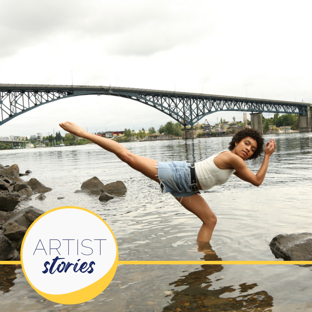 black woman wearing a white tank top and denim shorts doing a balletic pose in a river with a bridge in the background